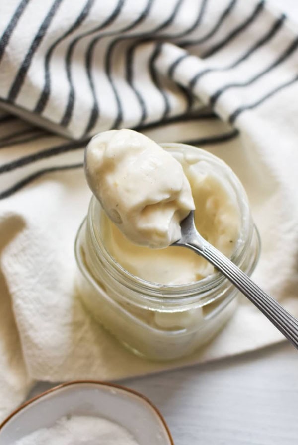 A spoon with eggless mayo on it resting on top of a mason jar.