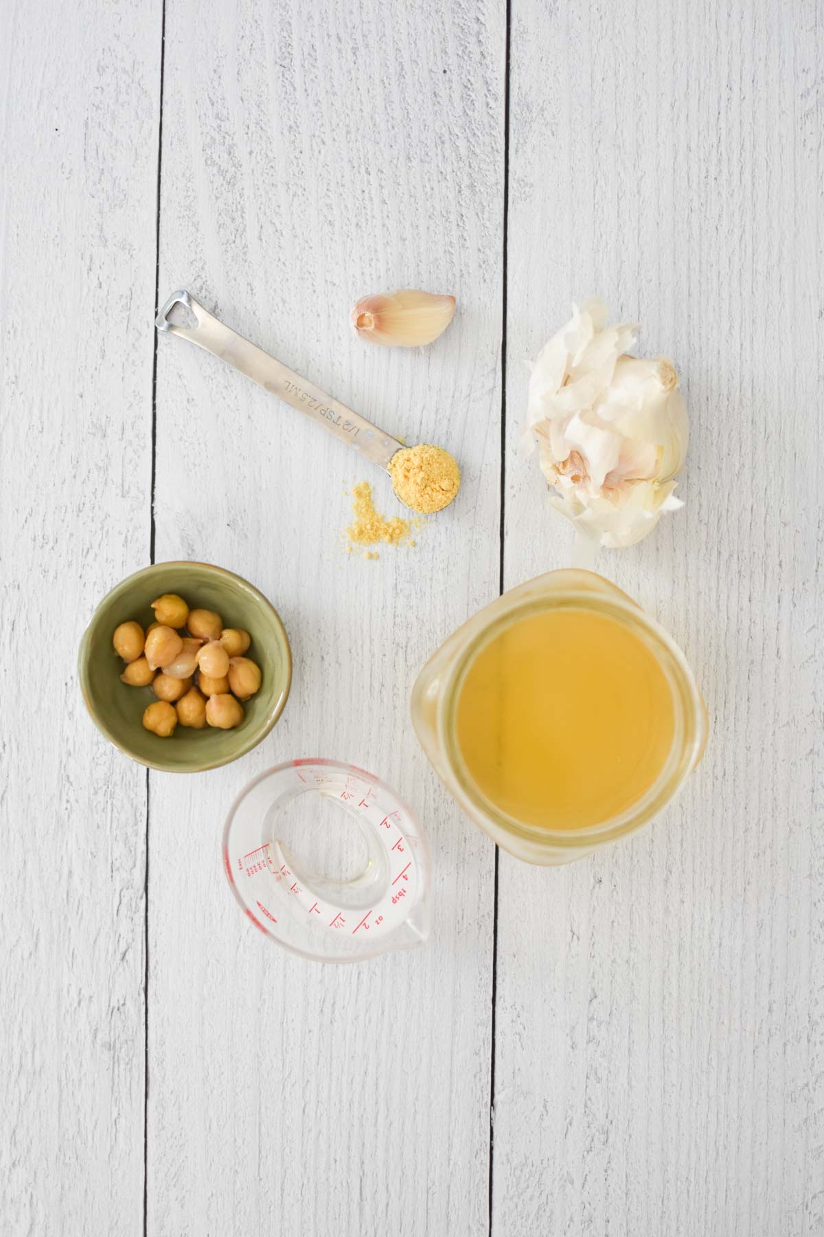 Chickpeas, aquafaba, garlic, mustard, and vinegar on a white wood table.