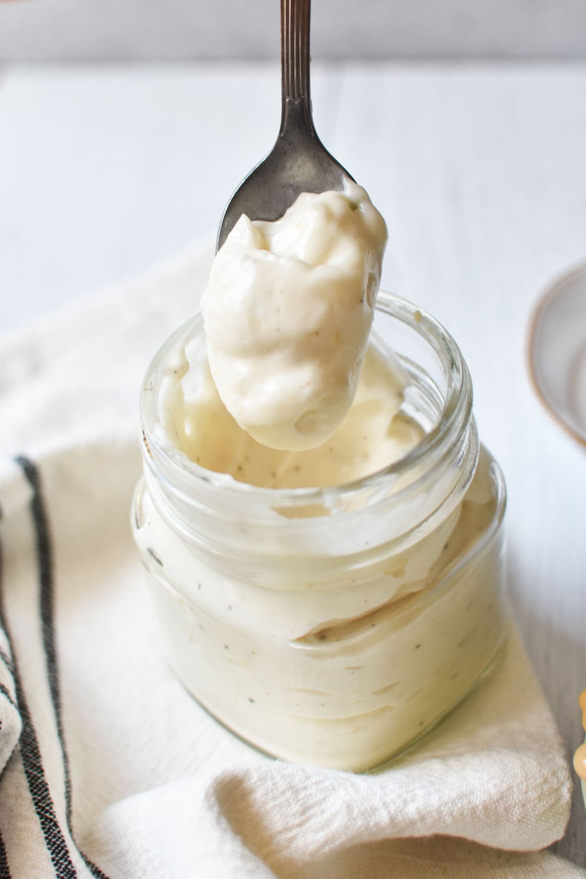 A spoon being dipped into thick egg free mayo in a mason jar.