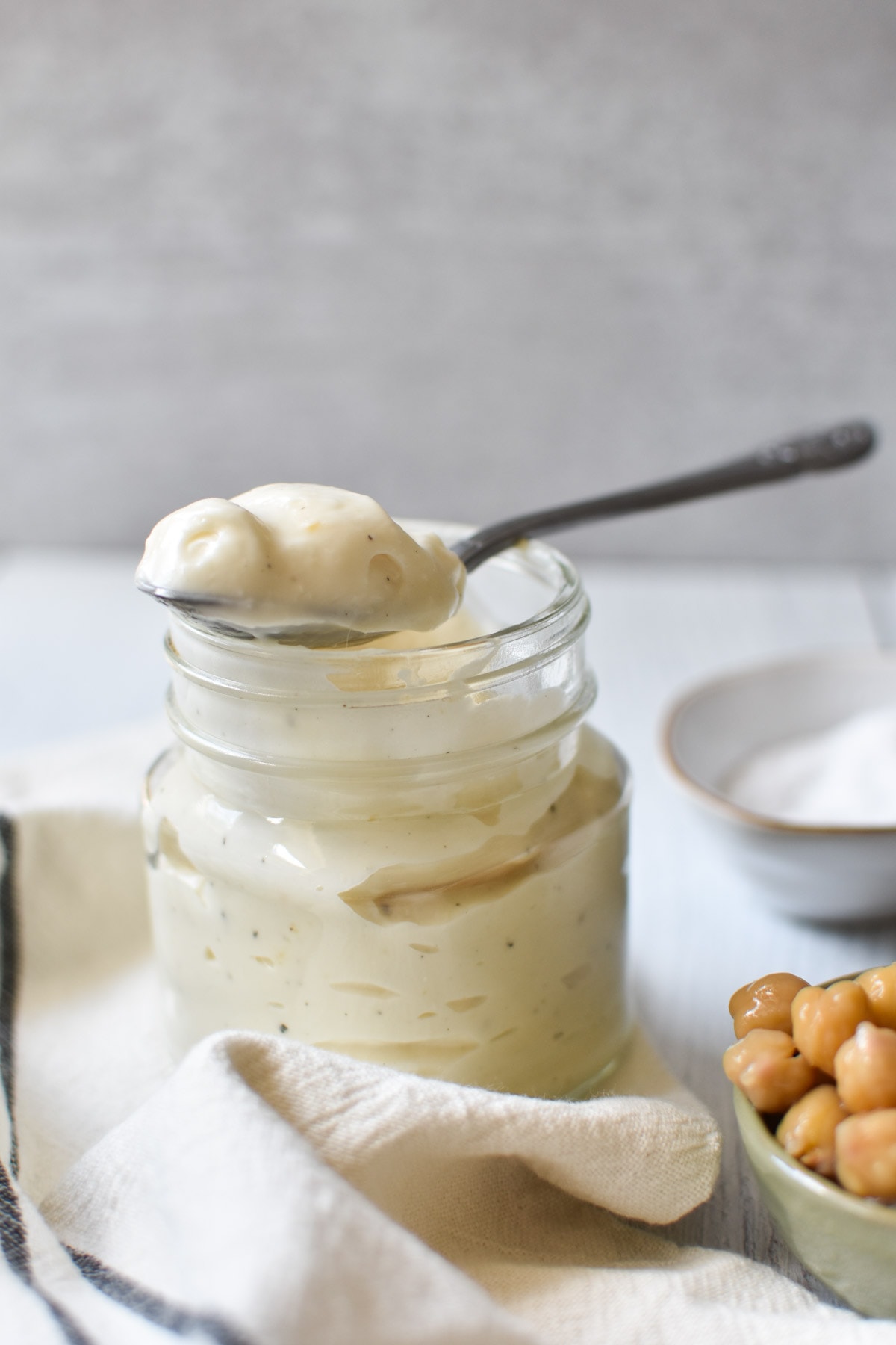 A mason jar of mayonnaise next to a cup of chickpeas and salt.
