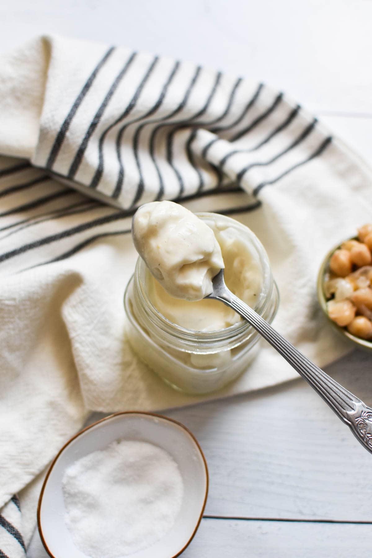 A spoon resting on top of a jar of egg free mayo next to chickpeas.