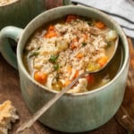 Chicken and brown rice soup in a large green bowl with a spoon.