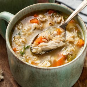 A spoon scooping chicken and brown rice soup with carrots and celery.