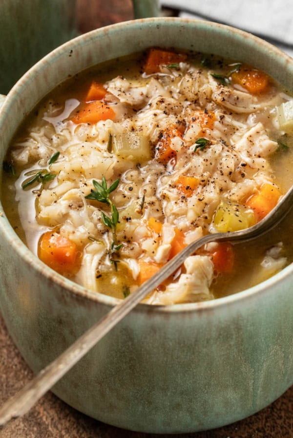 Chicken and brown rice soup in a large green bowl with a spoon.