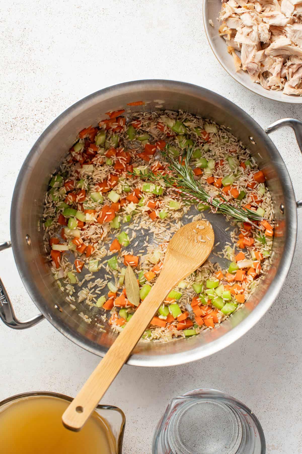 Adding brown rice and herbs to the soup pot with vegetables.
