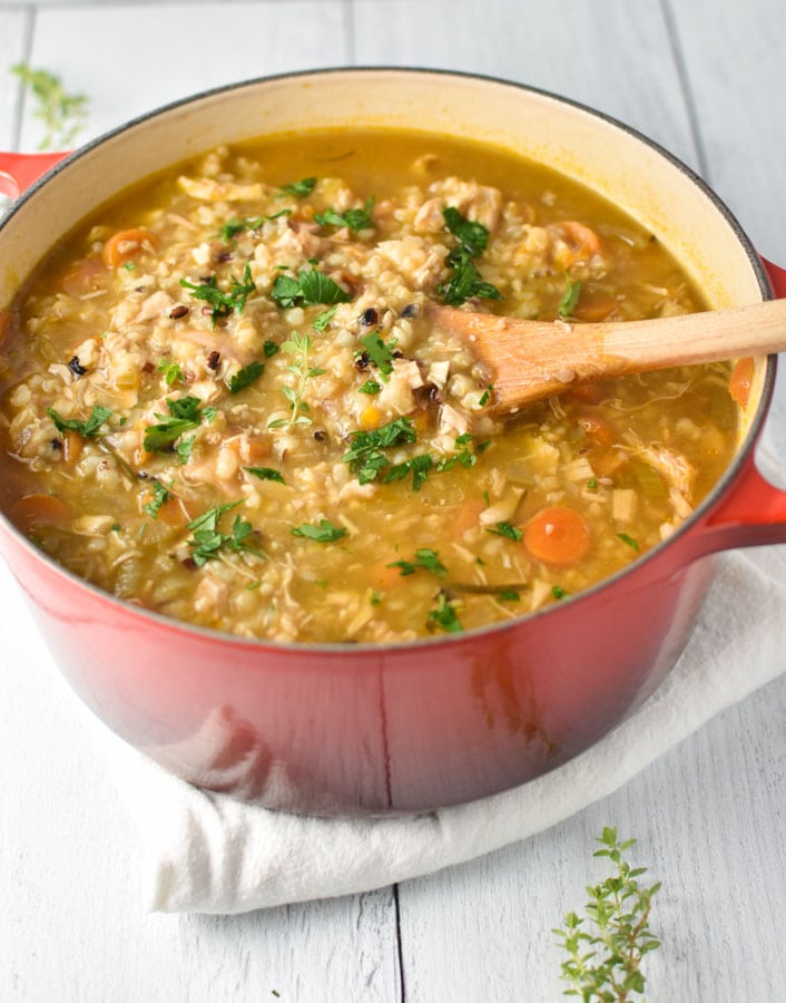 a wooden spoon scooping chicken and rice soup from a big red pot