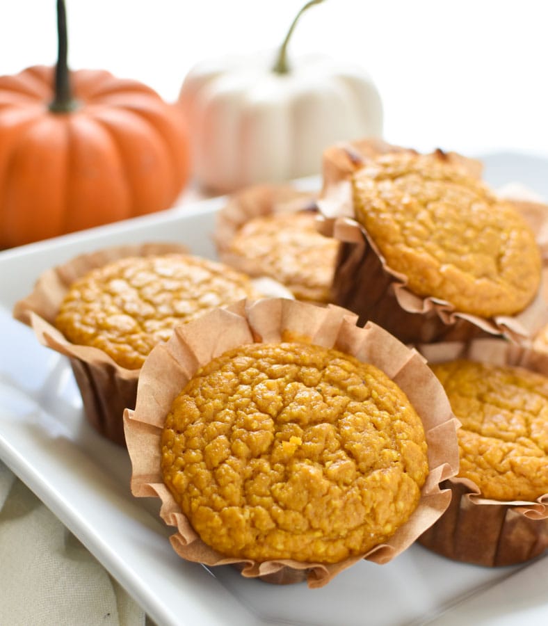 pumpkin cornbread muffins in paper cups stacked with mini pumpkins in the back