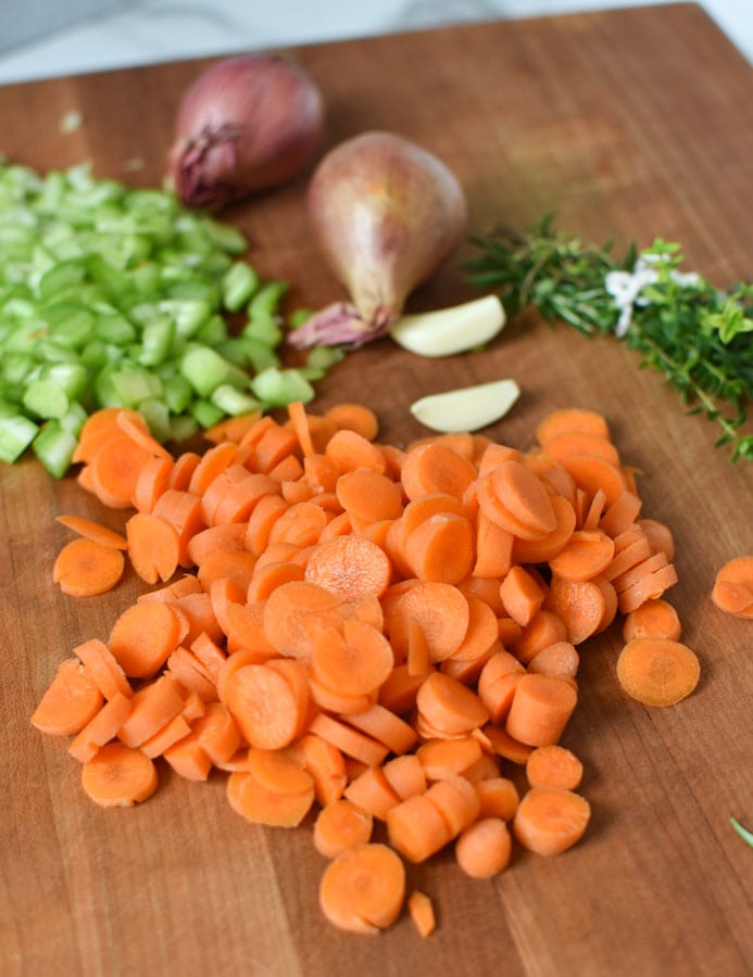 chopped carrots, celery, garlic, and herbs on a board