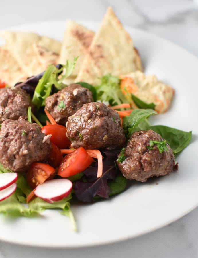 meatballs in a greek salad with pita and hummus on a white plate