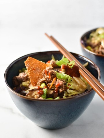 an egg roll bowl with a wonton chip and sriracha on top with chopsticks