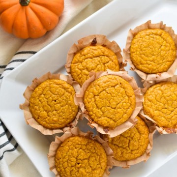 pumpkin cornbread muffins stacked on a white plate next two two pumpkins