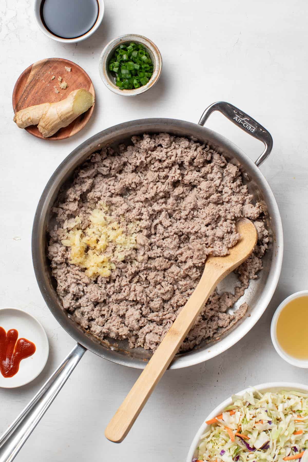 Adding garlic and ginger to the ground turkey in a pan.