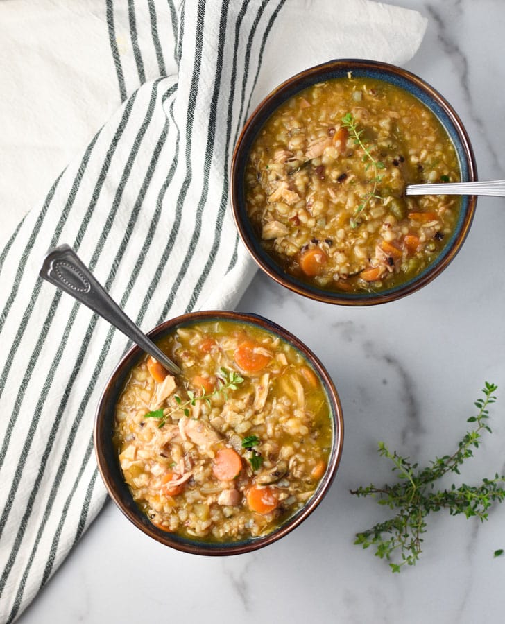 two bowls of chicken and brown rice soup with thyme and spoons