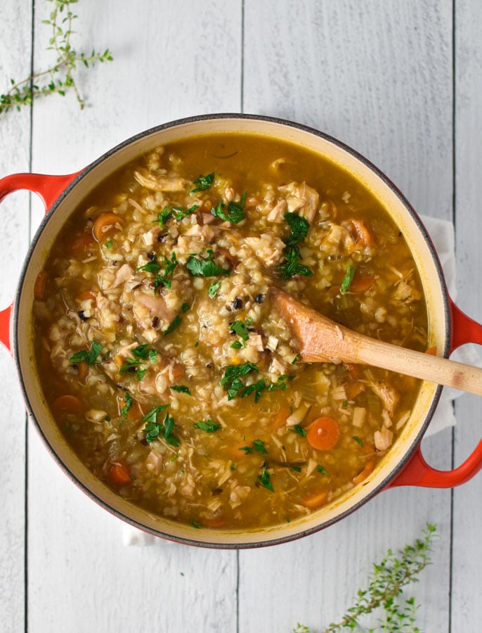 a pot of chicken and rice soup on a white board with thyme sprigs