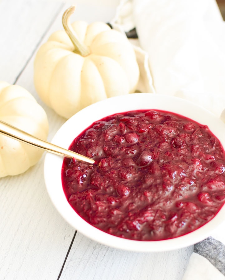 Cranberry sauce in a white bowl with white pumpkins in the background.