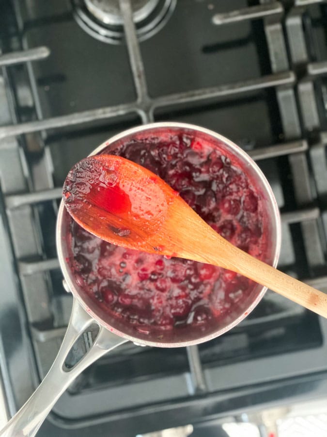 cranberry sauce being boiled in a pot with a wooden spoon