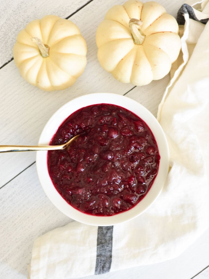 cranberry sauce in a white bowl on a towel with a gold spoon and white pumpkins