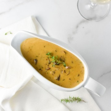 mushroom gravy in a white gravy boat with a napkin and glass of wine