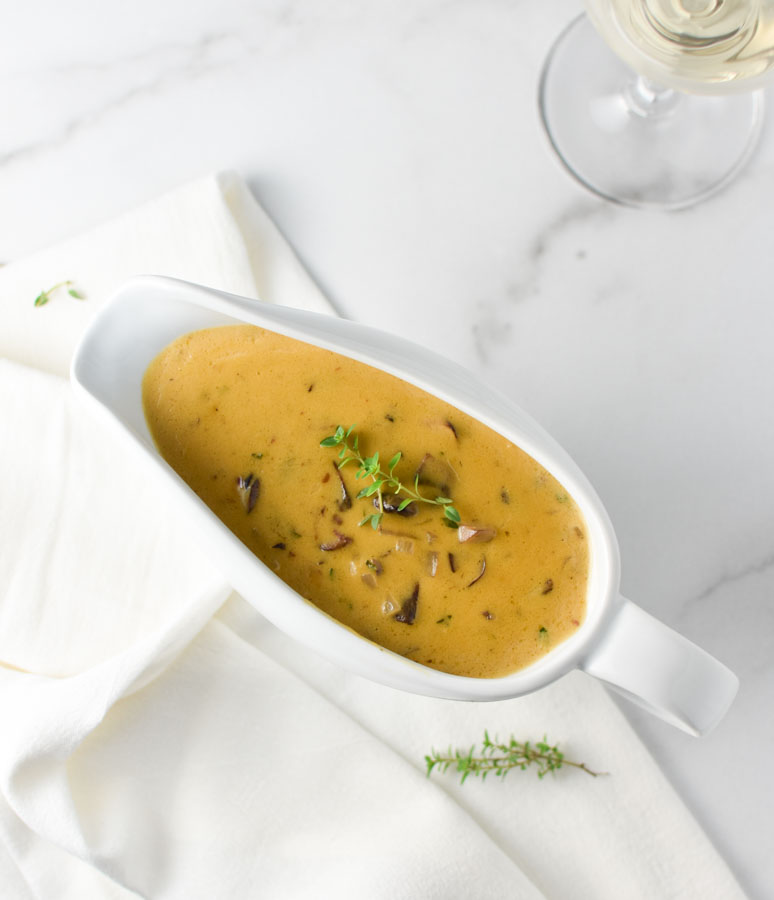 Mushroom gravy in a white gravy boat with a napkin and glass of wine.