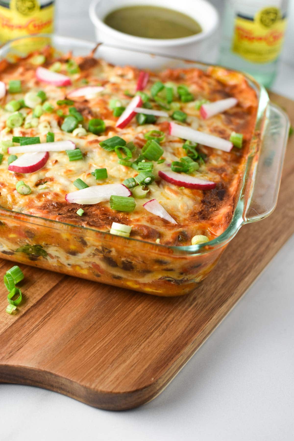 A turkey enchilada casserole next to salsa verde and two topo chico bottles