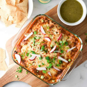 A ground turkey enchilada casserole on a cutting board with salsa verde and chips