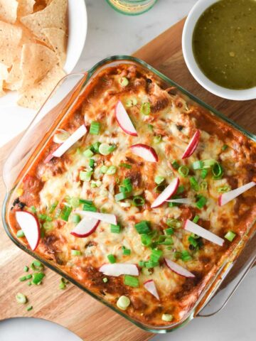A ground turkey enchilada casserole on a cutting board with salsa verde and chips