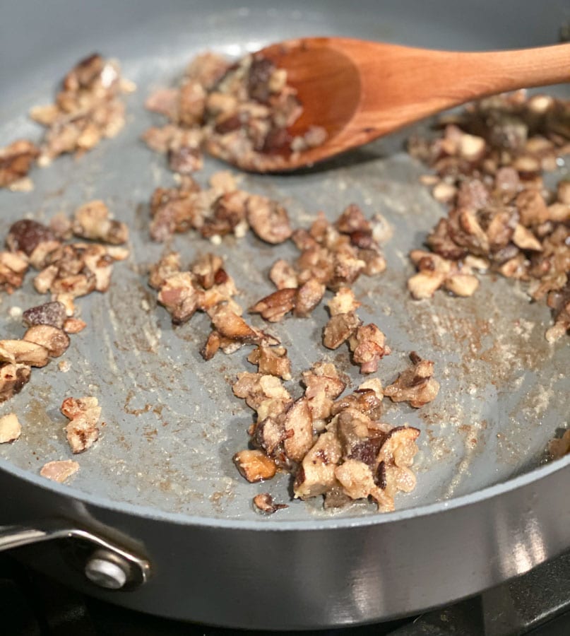 mushrooms being sautéed in a pan with a wooden spoon