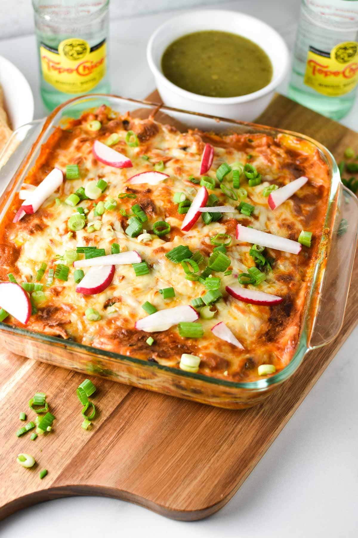 An up close view of an enchilada casserole with melted cheese, green onions, and radish on top.