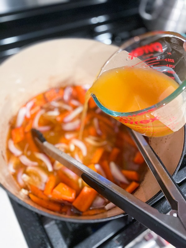 Pouring broth into a Dutch oven filled with vegetables.