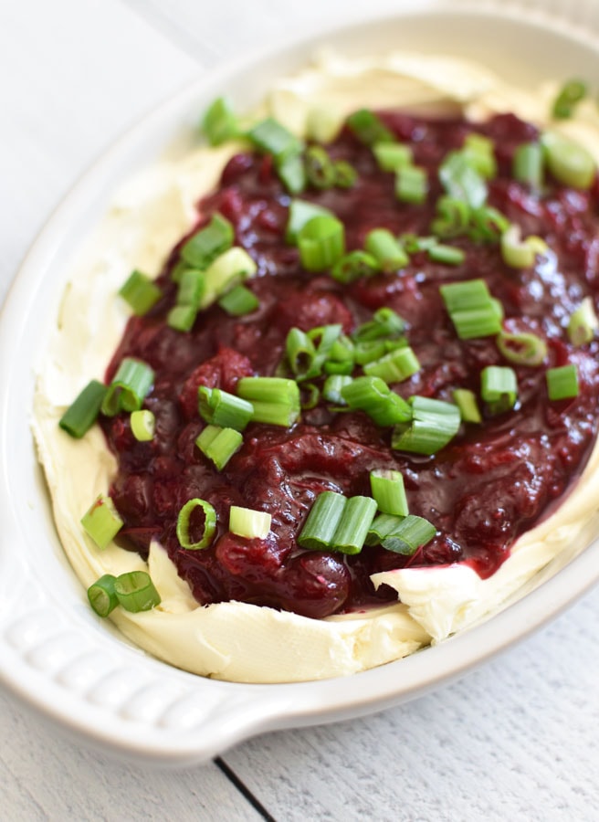 A white bowl of cranberry jalapeno cream cheese dip topped with scallions