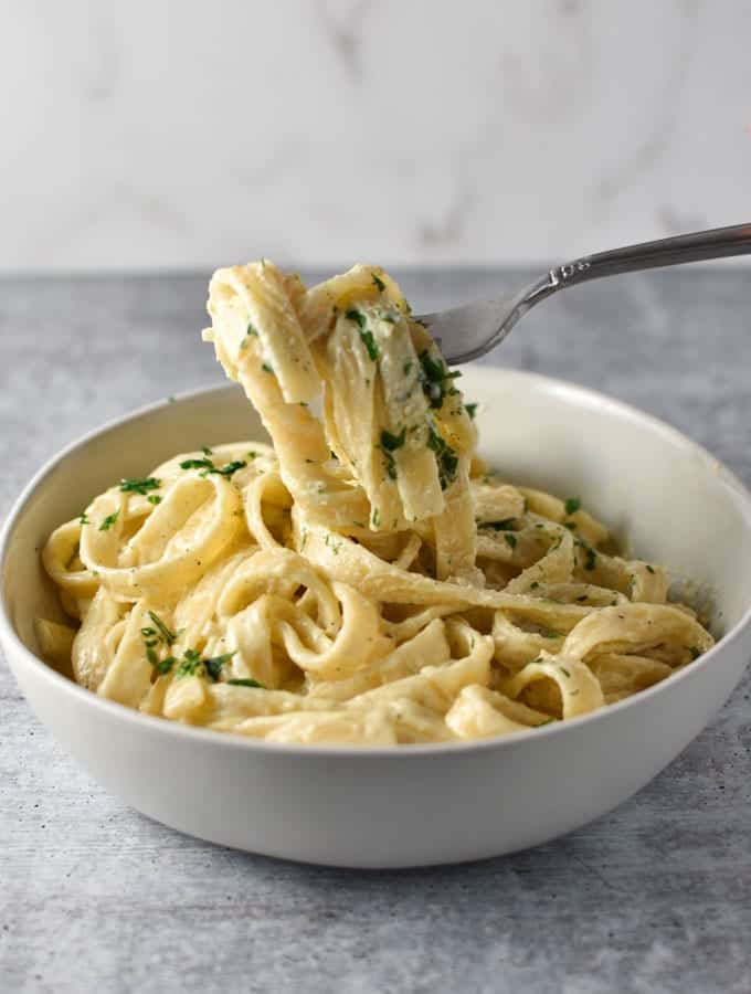 těstoviny Fettuccine Boursin omotané kolem vidlice, která se zvedla nad velkou bílou misku těstovin. Petržel je posypána nahoře.'s lifted above a big white bowl of pasta. Parsley is sprinkled on top.