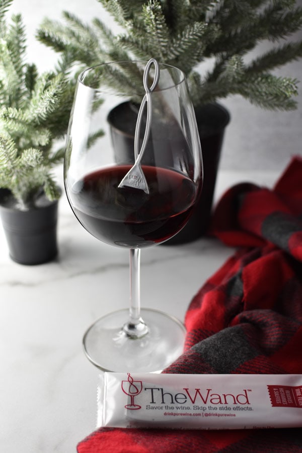 A glass of red wine in front of two small Christmas trees.