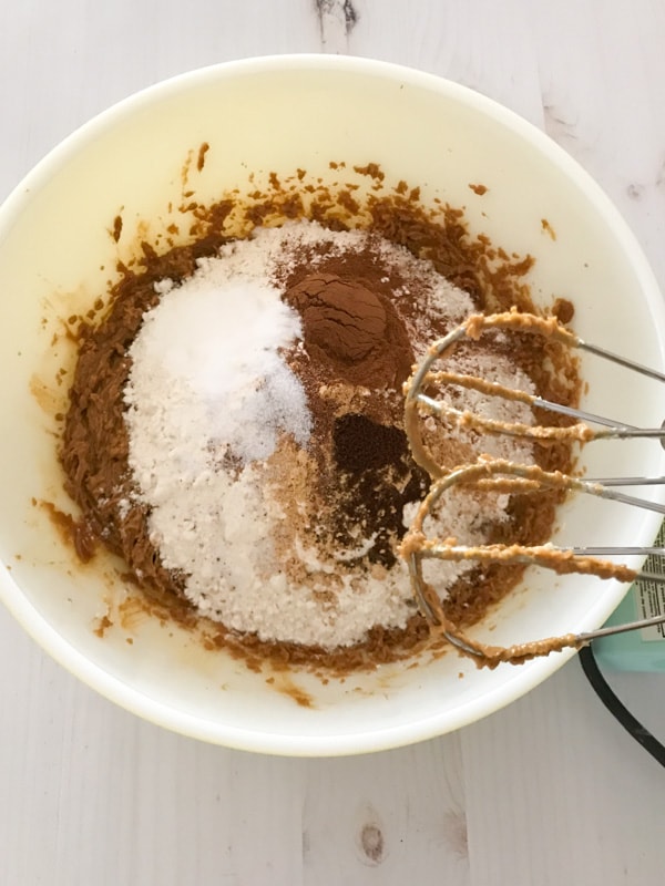 A mixer over a bowl of gingerbread dough ingredients