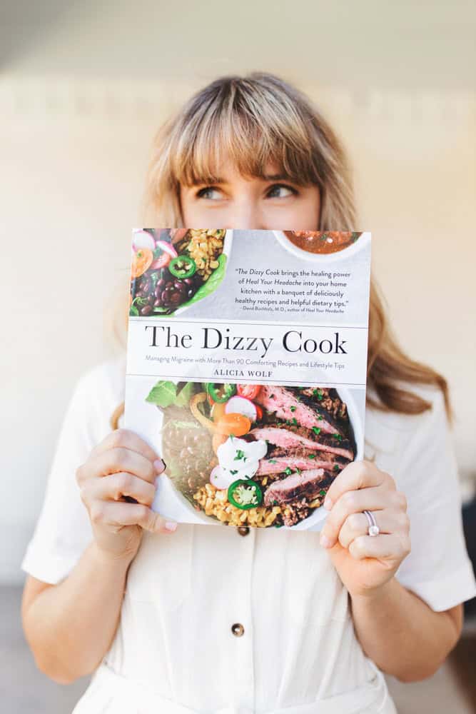 A girl holding The Dizzy Cook Cookbook in a white dress