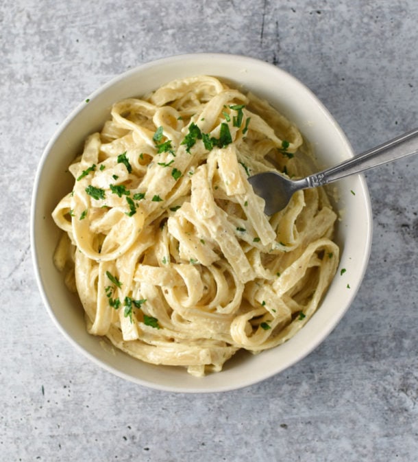 An overhead shot of a big bowl of creamy pasta with a fork in it on a gray table