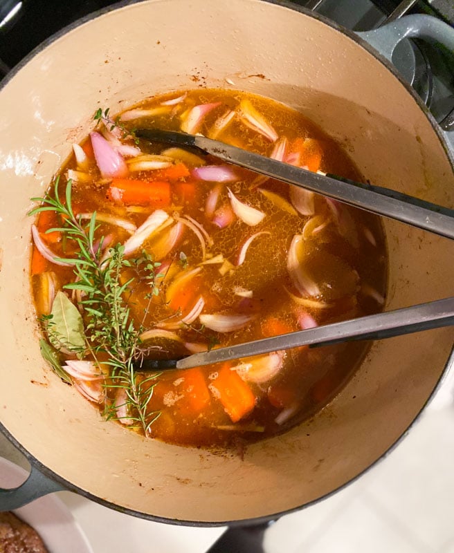 Broth, vegetables, and herbs simmering in a dutch oven. 