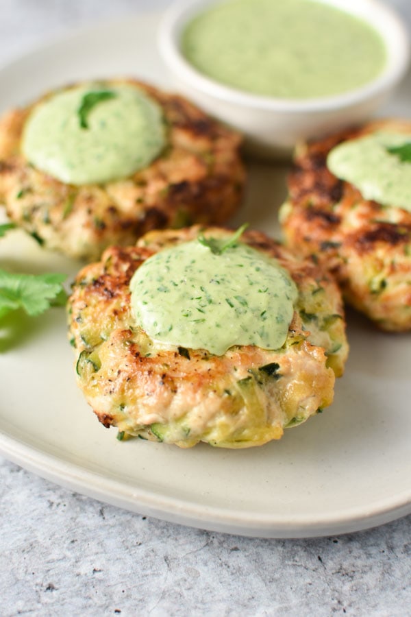 Three chicken zucchini bites with creamy cilantro sauce on the tops and a sprinkle of parsley