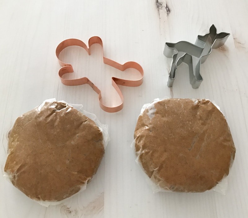 Cookie cutters next to two rolls of gingerbread cookie dough on a white table