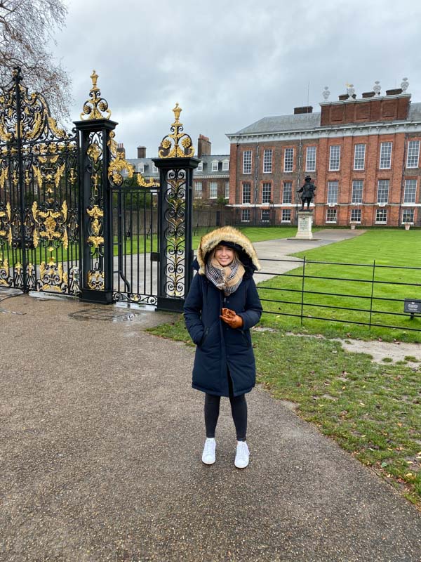 A girl in front of kensington palace with a large blue coat