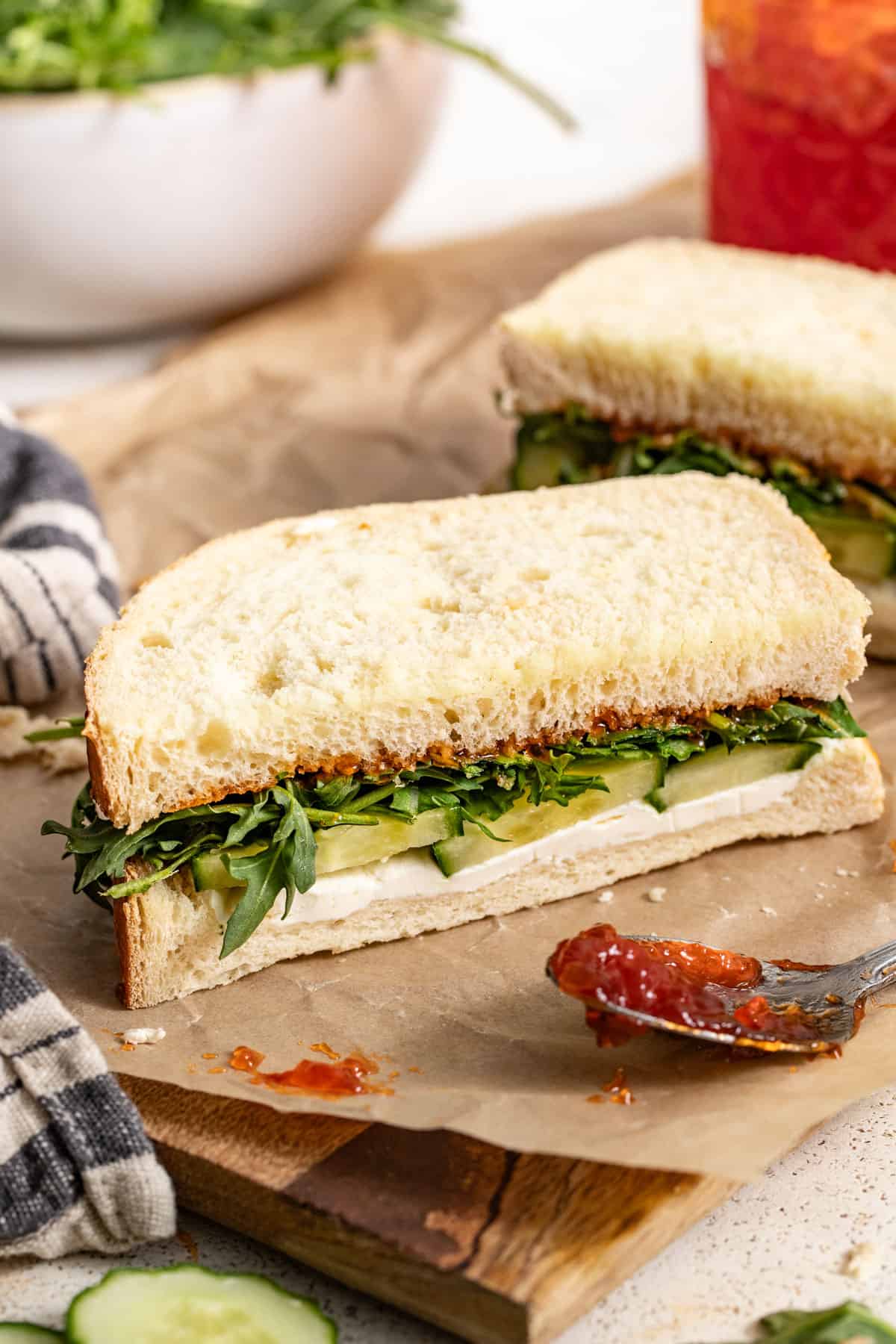 A goat cheese and arugula sandwich next to a spoon filled with pepper jelly.
