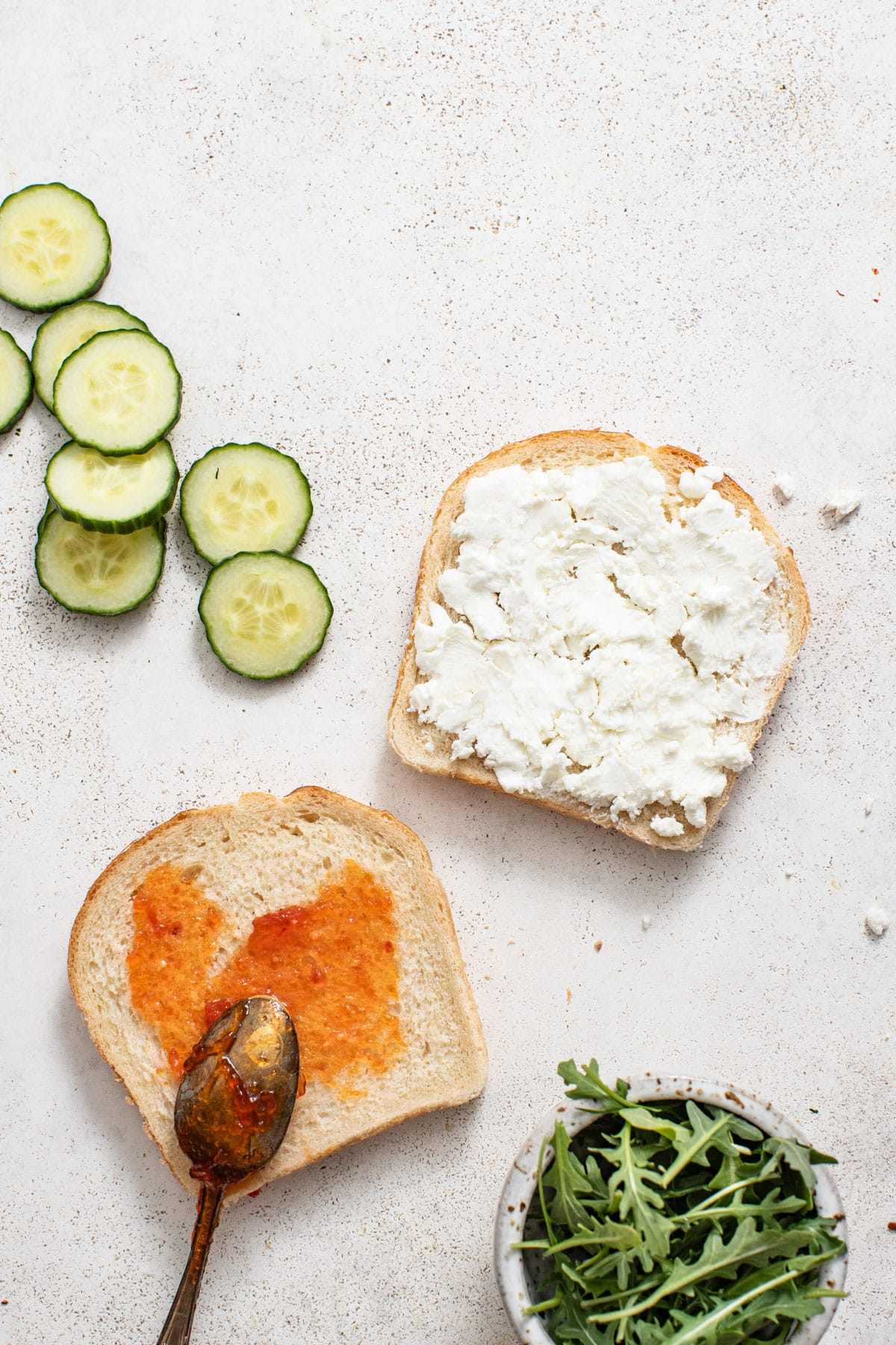 A spoon spreading jam on one side of the bread and goat cheese on the other.