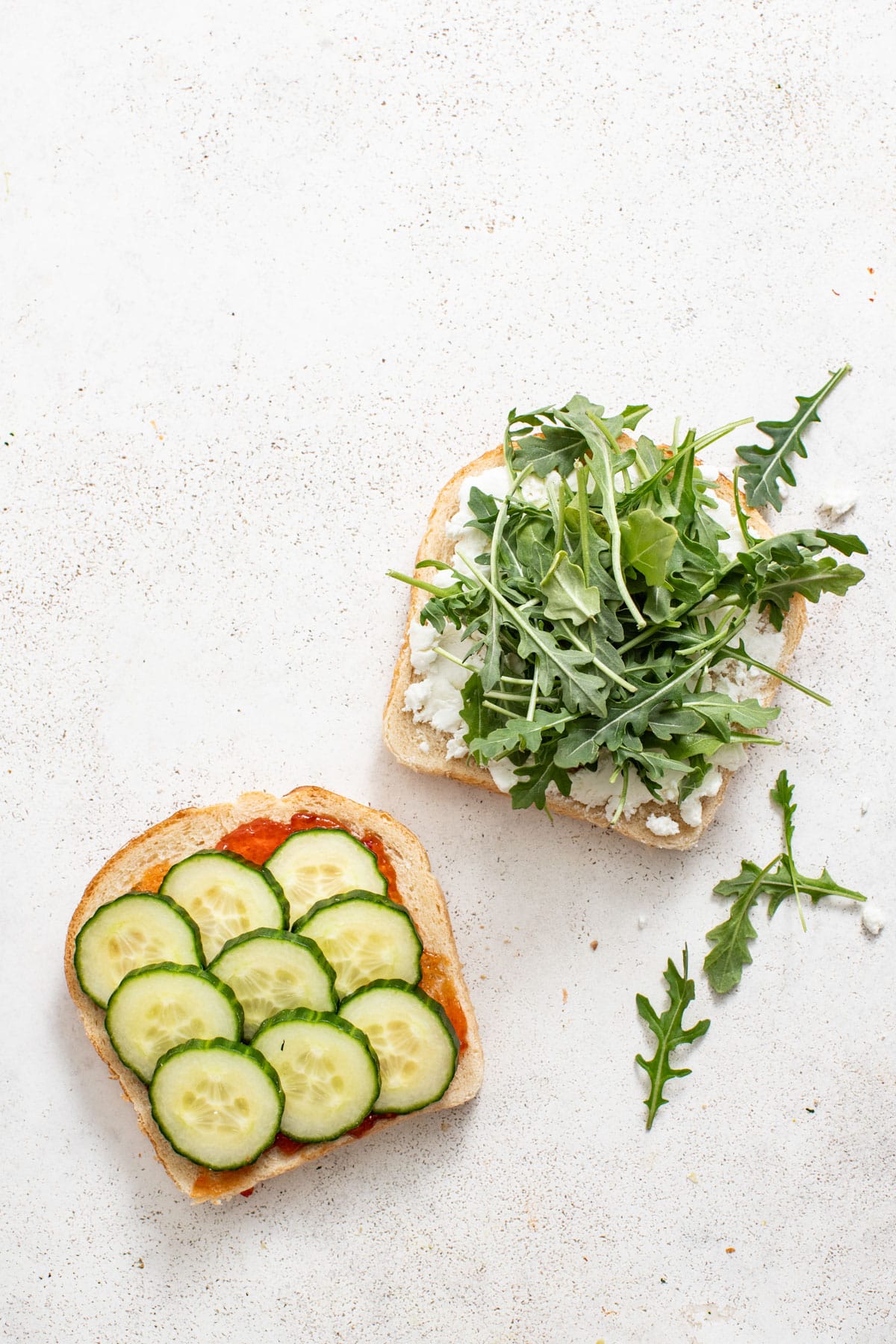 Layering cucumber and arugula on top of the cheese and bread.
