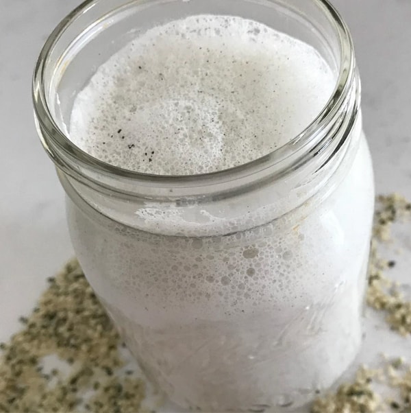 Homemade hemp milk in a mason jar on a white table with hemp seeds around it