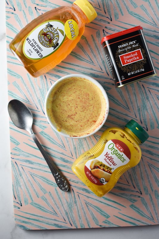 Honey, mustard, paprika, on a patterned cutting board with a bowl of honey mustard sauce