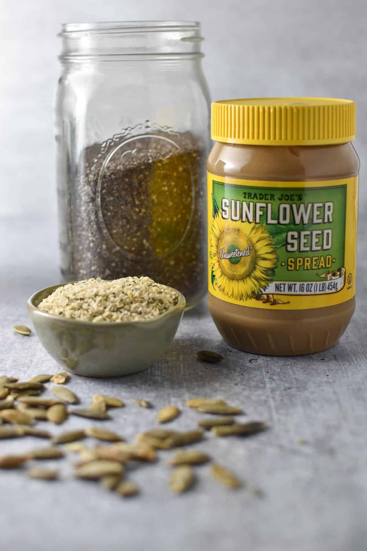 A mason jar with chia seeds next to sunflower seed butter and hemp seeds.