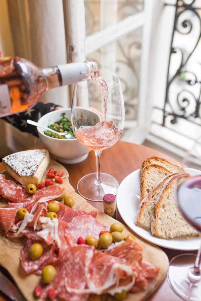 A bottle of wine being poured next to a cheese tray and olives