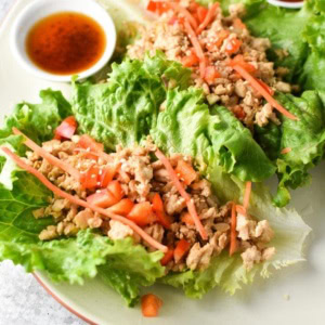 Thai Chicken Lettuce Wraps on a plate topped with carrots, peppers, and a sauce on the side