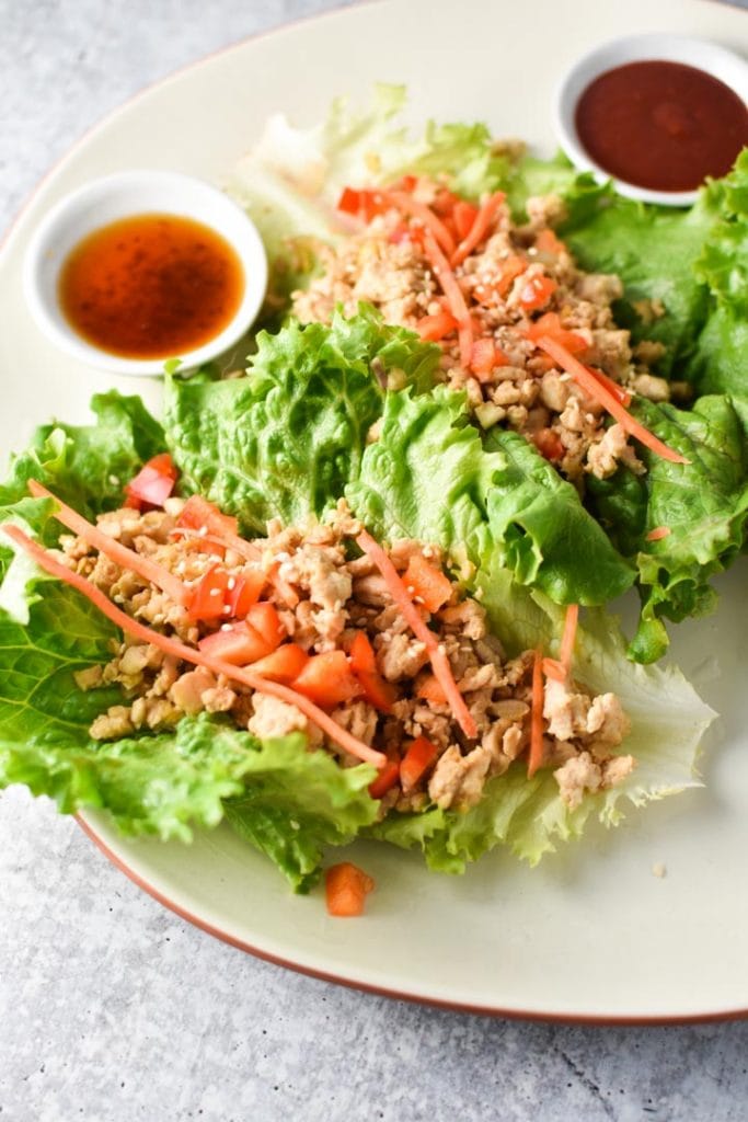 Thai Chicken Lettuce Wraps on a plate topped with carrots, peppers, and a sauce on the side