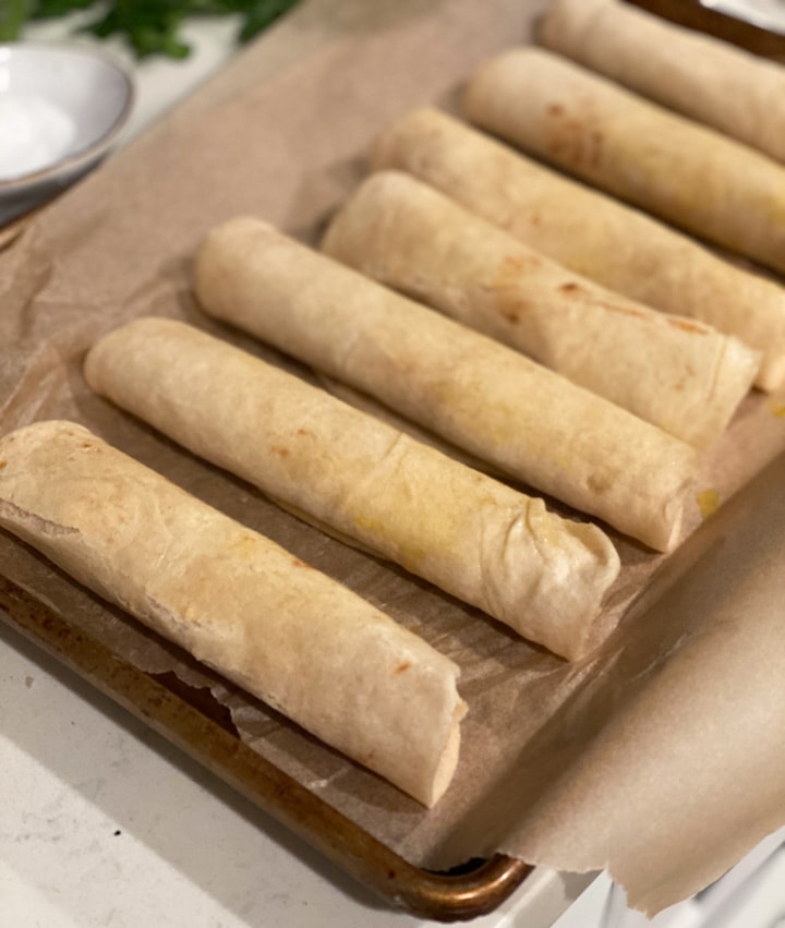 Unbaked creamy chicken taquitos on a baking sheet