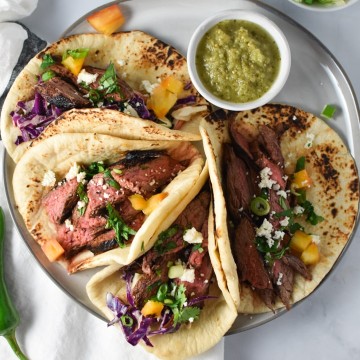 Steak tacos on a grey plate with salsa verde